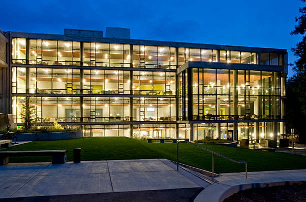UCSC McHenry library, lit up at dusk. It's a four-story structure and all the lights are on in the nearly floor-to-ceiling windows.